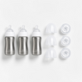 Three stainless steel baby bottles with white caps and three clear accessories arranged on a clean white background.