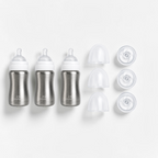 Three stainless steel baby bottles with white caps and three clear accessories arranged on a clean white background.